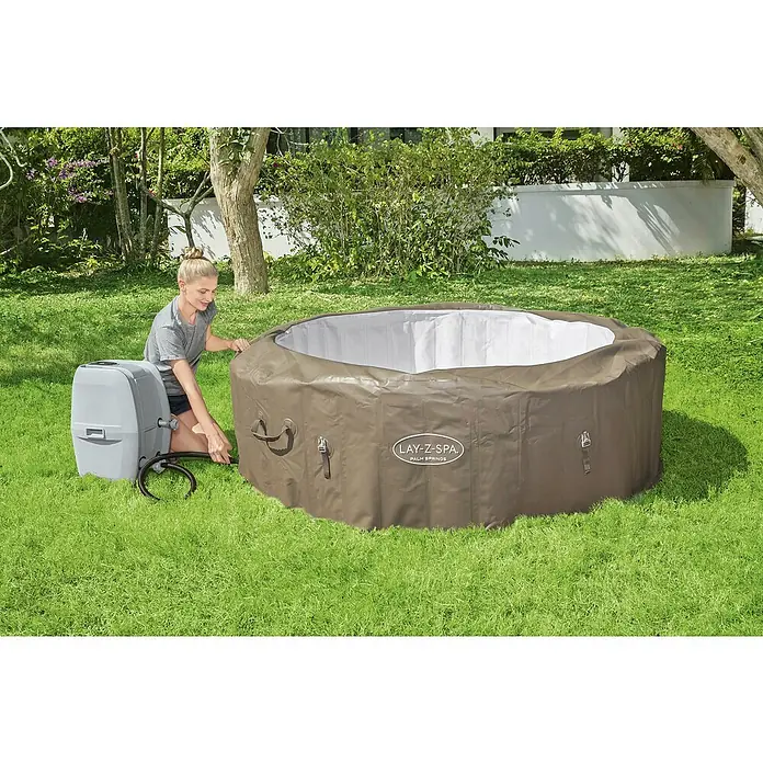 Bestway Lay-Z-Spa Mobil-Whirlpool Palm Springs - Ø x H: 196 x 71 cm, Taupe, 916 l - Eine Frau schließt einen Lay-Z-Spa Whirlpool an. Der Whirlpool ist braun und steht auf einer grünen Wiese.