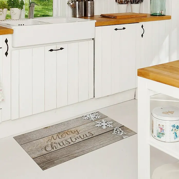 Alfombra de vinilo Croma Winter - Marrón, 75 x 45 cm - Una alfombra de cocina rectangular con un diseño de madera navideño y adornos de copos de nieve, colocada frente a gabinetes de cocina blancos.