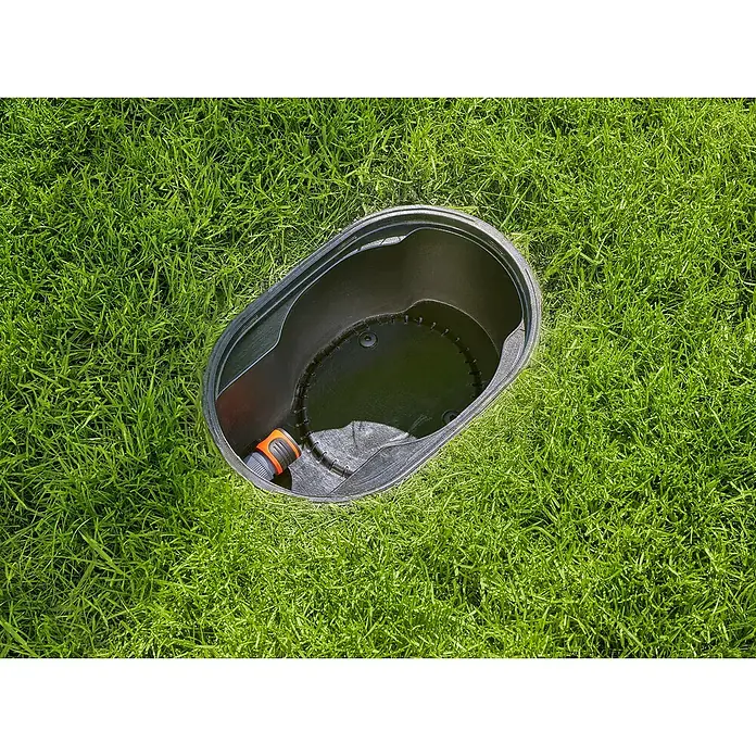Gardena Sprinklersystem Bewässerungsanschlussbox - Passend für: Gardena Versenkregner AquaPrecise & Gardena Pipeline, Größe Anschluss: ¾″ - Ein Rasenmähroboter-Garage aus schwarzem Kunststoff steht im grünen Gras. Der Roboter-Unterstand hat einen Schlauchanschluss für die Reinigung.