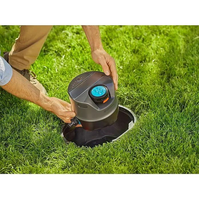 Gardena Sprinklersystem Versenkregner-Set AquaPrecise Basis - Max. Regnerfläche: 320 m², Reichweite ca.: 2 m - 10 m - Nahaufnahme einer Person, die einen GARDENA Sprinkler in eine unterirdische Anschlussdose im Rasen einsetzt.