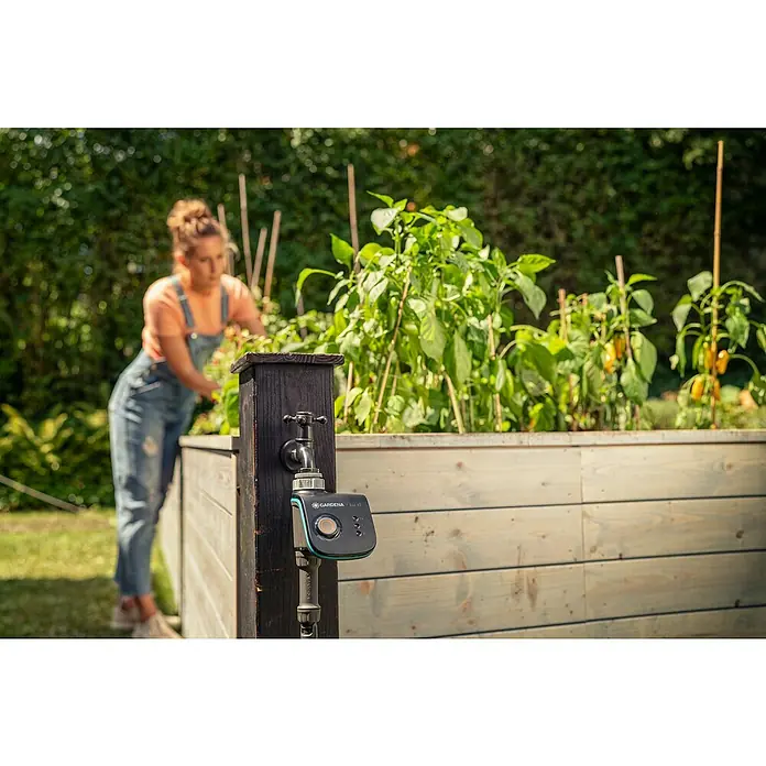 Gardena Smart system Bewässerungsautomat Smart Water Control - Betriebsdruck: 0,5 bar - 12 bar, Bewässerungsdauer: 1 min - 10 h - Ein Gardena Bewässerungsautomat Select mit praktischem Wasserhahn in einem Gartenbeet, bedient von einer Gärtnerin.