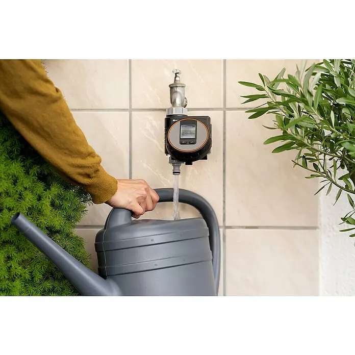Gardena Bewässerungscomputer Flex - Bewässerungsdauer: 1 s - 99 min - Eine Person füllt eine graue Gießkanne mit einem Gardena Bewässerungscomputer an einem Wasserhahn, um Pflanzen zu gießen.