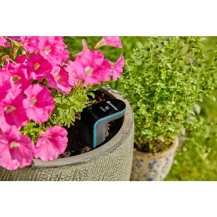 Gardena Smart system Bodenfeuchtesensor - Passend für: Gardena Smart System Sets - Nahaufnahme eines Gardena Smart Sensors im Topf mit pinkfarbenen Blüten und grünen Pflanzen, zur Messung der Bodenfeuchtigkeit.