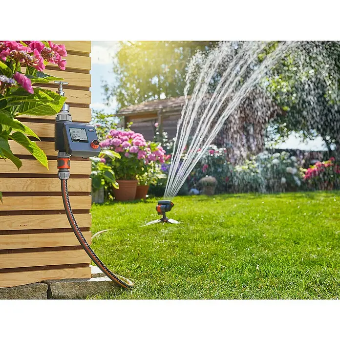 Gardena Bewässerungscomputer Select - Bewässerungsdauer: 1 min - 3 h - Der Gardena Bewässerungscomputer im Einsatz, um den Rasen zu bewässern, mit Blumen und Sträuchern im Hintergrund.