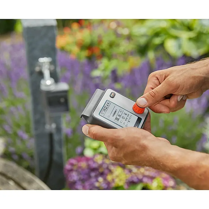 Gardena Bewässerungscomputer Master - Bewässerungsdauer: 1 s - 99 min - Nahaufnahme der Gardena Bewässerungssteuerung, die in den Händen einer Person gehalten wird, mit einem Wasserhahn im Hintergrund.