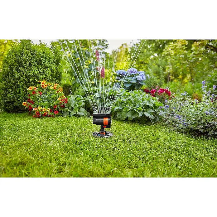 Gardena Sprinklersystem Viereckregner - Max. Regnerfläche: 216 m² - Gardena Vielflächenregner AquaZoom Compact im Einsatz, bewässert den Rasen vor üppiger Blumenpracht. Das Gerät ist schwarz-orange.