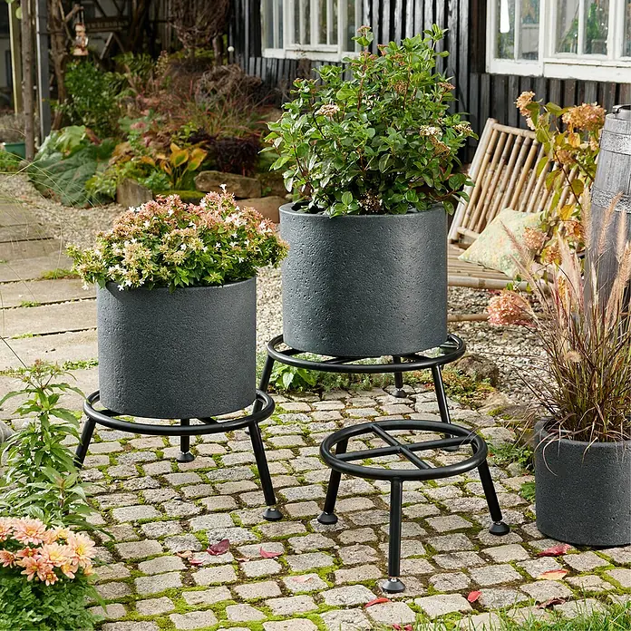 Wagner System Blumenständer - Ø x H: 38 x 25 cm, Stahl, Schwarz - Mehrere graue Pflanzgefäße mit Pflanzen auf schwarzen Metallständern im Garten.
