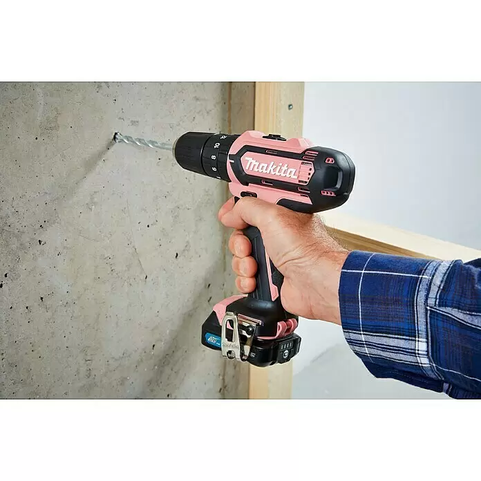 Makita Akku-Schlagbohrschrauber HP333DSAP1 - 12 V, 1 Akku, 2 Ah - Rosafarbener und schwarzer Makita Akku-Bohrschrauber wird von einer Hand gehalten und bohrt in eine Betonwand.