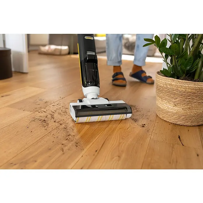 Kärcher Filter-Set - Passend für: Kärcher Saugwischer KFL 1, FCV 2 & FCV 3 - Der Kärcher Akku-Wischsauger entfernt Schmutz auf einem Holzboden, während eine Person im Hintergrund steht, neben einer Topfpflanze.
