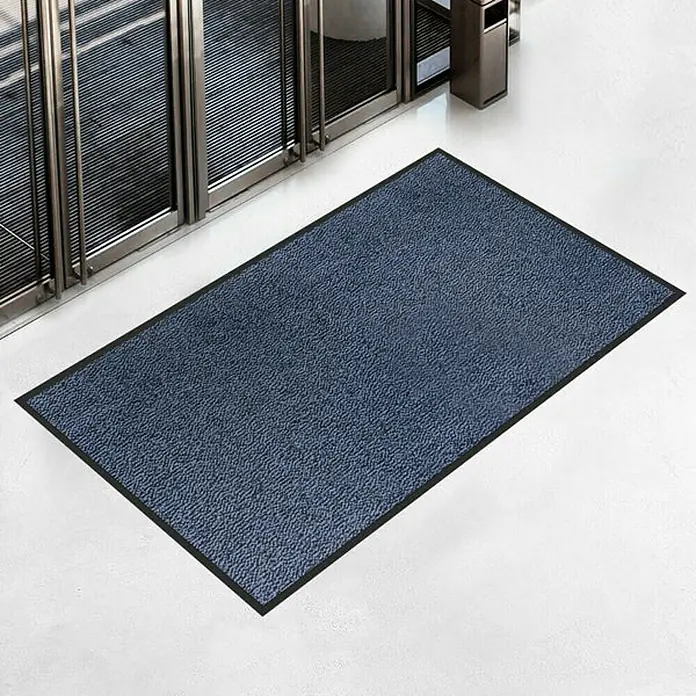 Fußmatte Sky - Blau, 200 x 135 cm, 100 % Polypropylen - Eine rechteckige, blaue Fußmatte mit schwarzem Rand liegt vor einem modernen Eingangsbereich, ideal zum Sauberhalten von Böden.