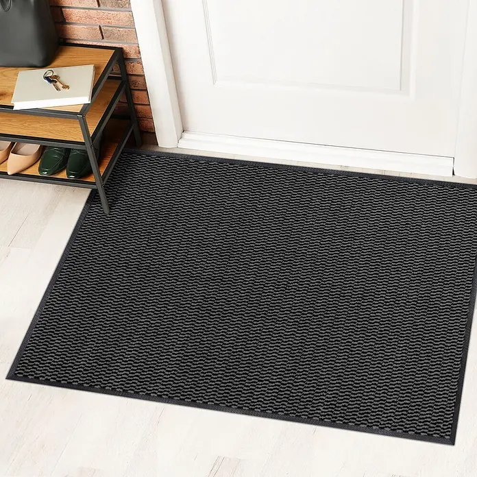 Fußmatte Sky Novo - Anthrazit, 90 x 60 cm, 100 % Polypropylen - Fußmatte in Schwarz mit gewelltem Muster vor einer Tür und einem Schuhregal.