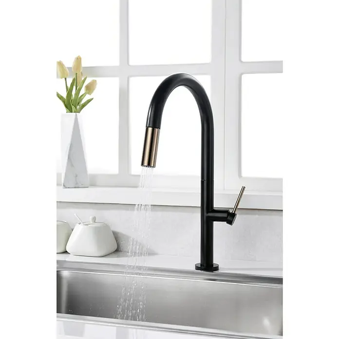 Imex Grifo de cocina extraíble Samoa - Negro/Oro rosa - Primer plano de un grifo de cocina negro con detalles dorados, con agua que fluye, sobre un fondo luminoso con una ventana.