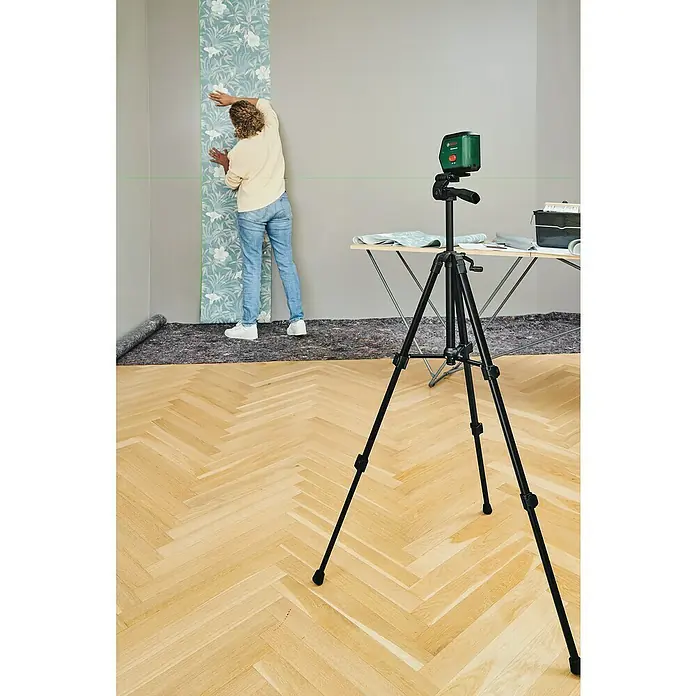 Bosch Stativ TT 120 - Höhenverstellung: 45 cm - 120 cm, Stativ-Gewinde: ¼″ - Eine Person bringt mit einem Bosch-Laserwerkzeug eine Tapete an einer Wand an, wobei ein Stativ für Stabilität sorgt.