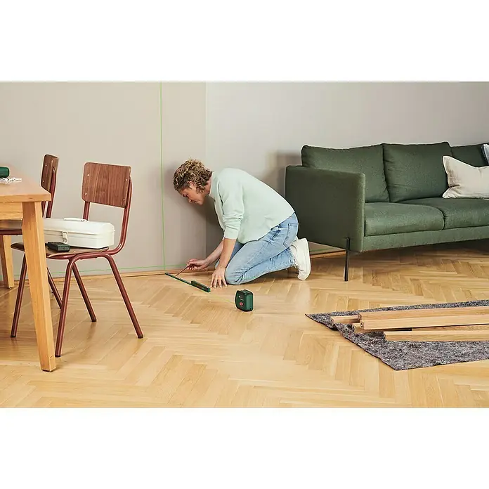 Bosch Kreuzlinienlaser Advanced Level 2G - Max. Arbeitsbereich: 15 m - Frau benutzt einen Bosch Kreuzlinienlaser, um eine gerade Linie an einer Wand zu markieren, während sie kniet und ein Lineal verwendet.