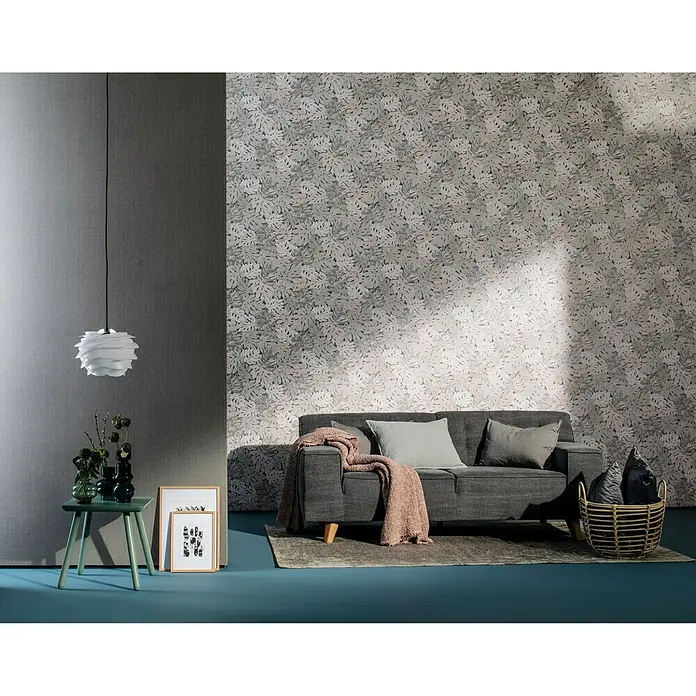 Marburg Casual Vliestapete Philodendron - Grau/Beige, Floral, 10,05 x 0,53 m - Ein stilvolles Wohnzimmer mit einem grauen Sofa, einem Beistelltisch und einer dekorativen Lampe, die eine gemütliche Atmosphäre schaffen.