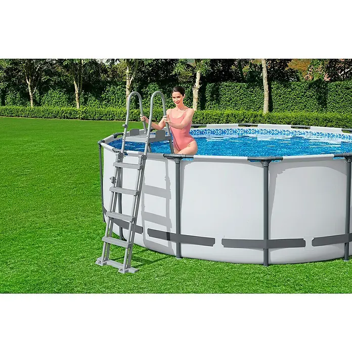 Bestway Frame-Pool Set Steel Pro Max - Ø x H: 549 x 122 cm, Lichtgrau, 23.062 l - Frau steigt mit einer Leiter in einen runden oberirdischen Pool mit weißer Verkleidung im Garten.