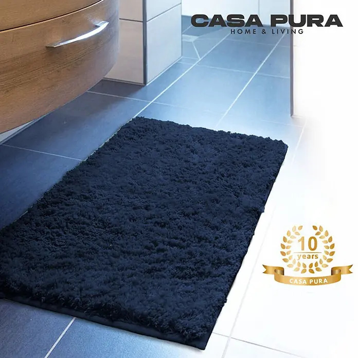 Floordirekt Badteppich Sky - 120 x 70 cm, Dunkelblau, 100% Polyester - Ein marineblauer Casa Pura Badteppich liegt auf einem hellen Badezimmerfliesenboden neben einem Waschbeckenunterschrank aus Holz.