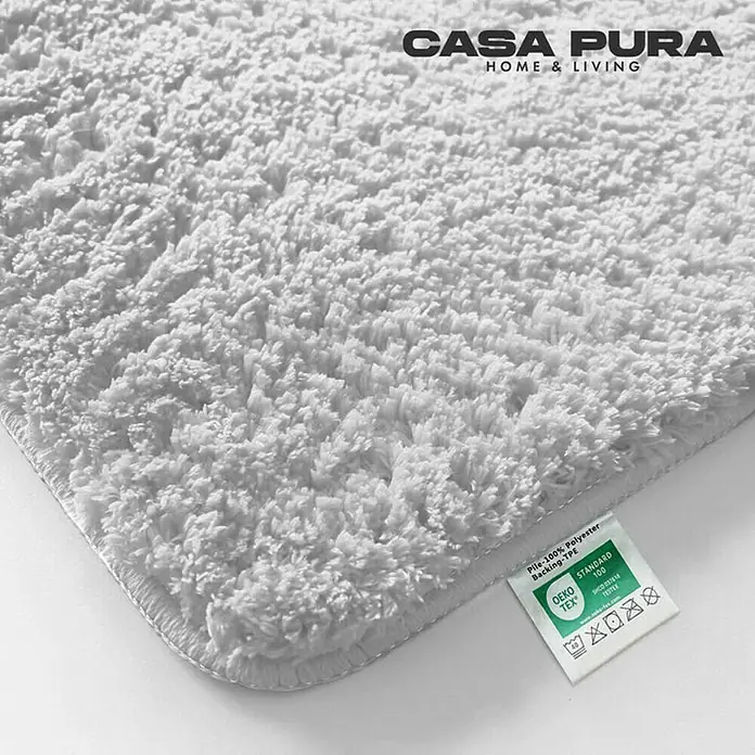 Floordirekt Badteppich Sky - 60 x 50 cm, Weiß, 100% Polyester - Nahaufnahme eines flauschigen, weißen Casa Pura Badezimmerteppichs mit Etikett, das die Materialzusammensetzung zeigt.