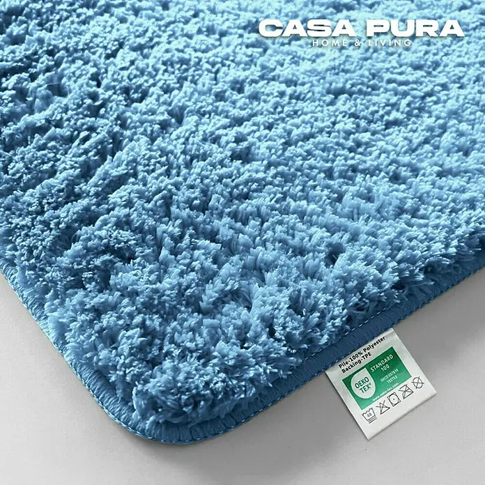 Floordirekt Badteppich Sky - 100 x 60 cm, Hellblau, 100% Polyester - Nahaufnahme eines blauen Casa Pura Teppichs mit weichen Fasern und Etikett, das die Materialzusammensetzung angibt.