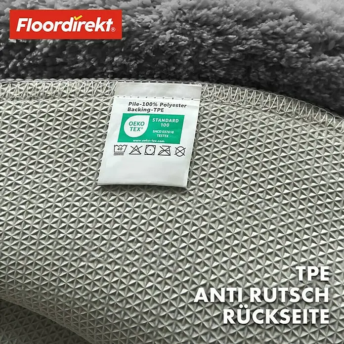 Floordirekt Badteppich Sky - 120 x 120 cm, Dunkelgrau, 100% Polyester - Detailaufnahme eines grauen Teppichs von Floordirekt mit Anti-Rutsch-Rückseite und Etikett, das die Materialzusammensetzung und Pflegehinweise zeigt.