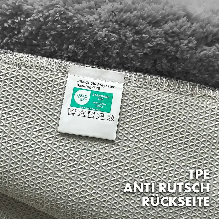 Floordirekt Badteppich Maris - 60 x 40 cm, Dunkelgrau, 100% Polyester - Detailansicht der Rückseite eines grauen Teppichs mit TPE-Antirutschbeschichtung und Etikett mit Produktdetails.