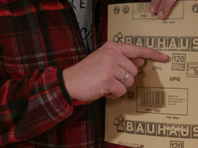 Mann zeigt auf die Körnung auf der Rückseite vom Schleifpapier