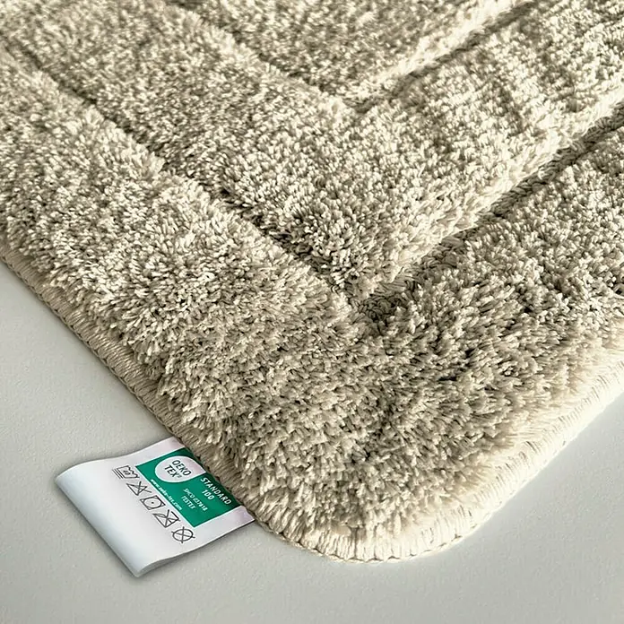 Floordirekt Badteppich Atlantis - 120 x 70 cm, Beige, 100% Polyester - Detailaufnahme einer beigefarbenen Badematte mit OEKO-TEX Standard 100 Etikett, die Weichheit und Qualität verspricht.