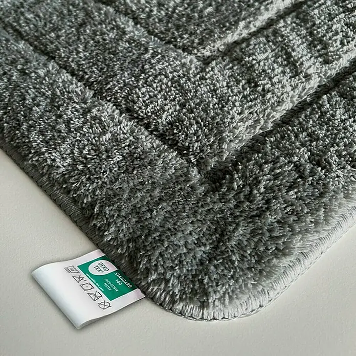 Floordirekt Badteppich Atlantis - 100 x 60 cm, Dunkelgrau, 100% Polyester - Detailaufnahme einer grauen Badematte mit OEKO-TEX Standard 100 Label, die Weichheit und Qualität des Materials hervorhebt.