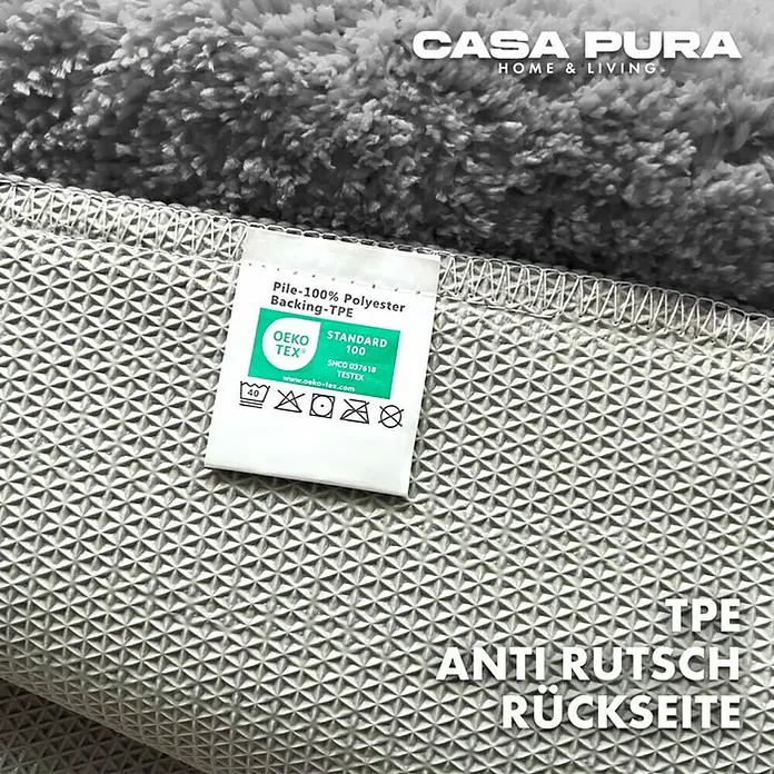 Floordirekt Badteppich Sky - 120 x 70 cm, Silbergrau, 100% Polyester - Detailaufnahme eines Casa Pura Teppichs, der die Rückseite mit Anti-Rutsch-Beschichtung und das Etikett mit Materialzusammensetzung zeigt.