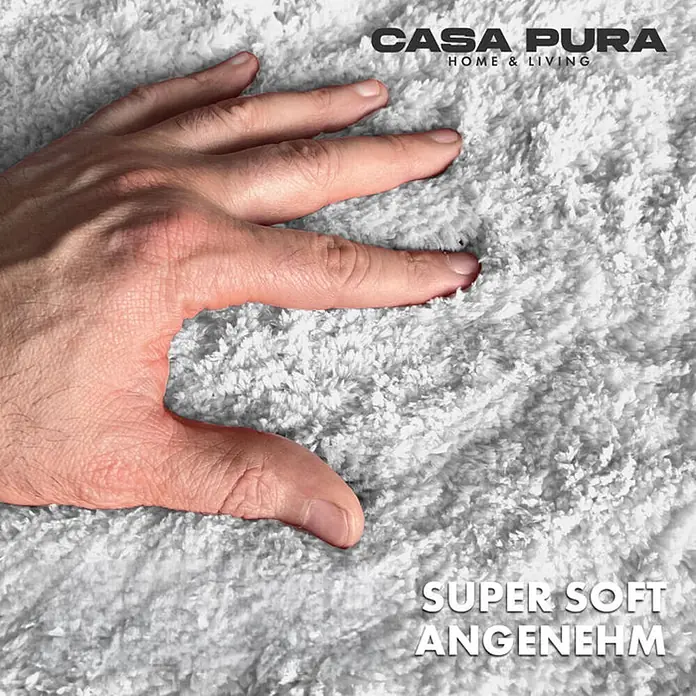 Floordirekt Badteppich Sky - 60 x 50 cm, Weiß, 100% Polyester - Nahaufnahme eines weichen, weißen Casa Pura Badteppichs. Die Hand berührt das flauschige Material. Geprüft auf Schadstoffe.