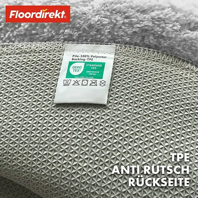 Floordirekt Badteppich Sky - 120 x 120 cm, Weiß, 100% Polyester - Detailaufnahme eines Teppichs von Floordirekt mit rutschfester TPE-Rückseite und einem Etikett, das die Materialzusammensetzung und OEKO-TEX® Standard 100 Zertifizierung ausweist.