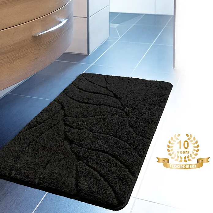 Floordirekt Badteppich Maris - 60 x 40 cm, Schwarz, 100% Polyester - Schwarze Badematte mit Blattmuster auf gefliestem Badezimmerboden, neben einem Waschtischunterschrank.