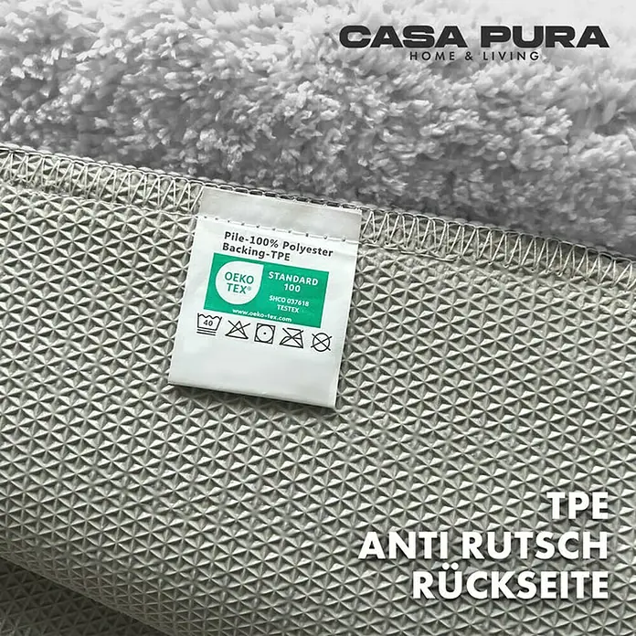 Floordirekt Badteppich Sky - 60 x 50 cm, Weiß, 100% Polyester - Detailansicht eines Teppichs mit TPE Anti-Rutsch Rückseite, inklusive Etikett mit Pflegehinweisen und Materialzusammensetzung.