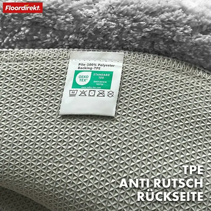 Floordirekt Badteppich Maris - 120 x 120 cm, Silber, 100% Polyester - Detailansicht eines grauen Teppichs mit rutschfester TPE-Rückseite und einem Etikett, das die Materialzusammensetzung und Zertifizierung bestätigt.
