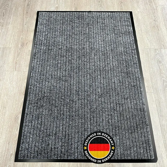Fußmatte Dura - Anthrazit, 150 x 90 cm, 100 % Polypropylen - Ein grauer Fußabtreter mit dem Aufdruck "Designed in Germany" liegt auf einem hellen Holzboden.