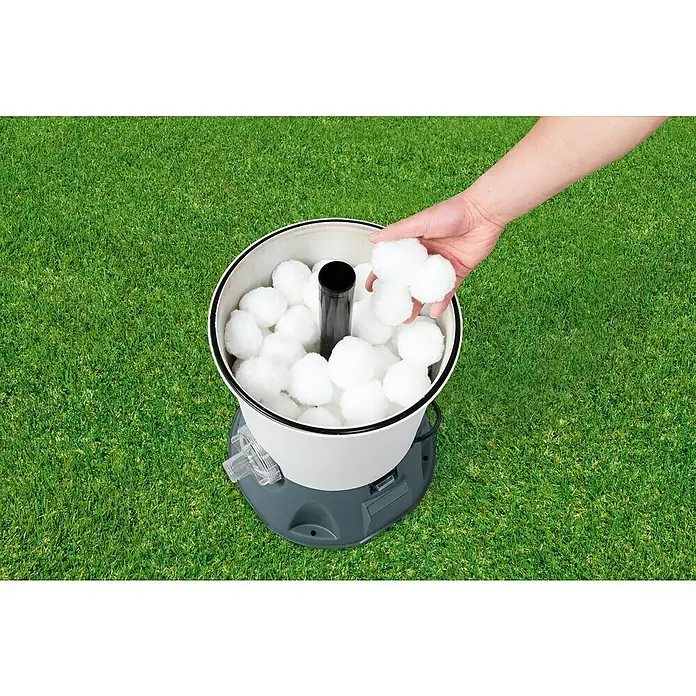 Bestway Flowclear Filterbälle - 500 g - Befüllung eines Poolfilters mit Filterbällen. Der Filter steht auf Rasen, und eine Hand füllt weiße Filterbälle ein.