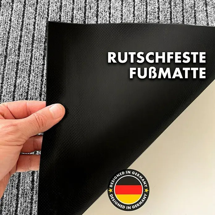 Fußmatte Dura - Grau, 120 x 66 cm, 100 % Polypropylen - Bild einer rutschfesten Fußmatte, die in Deutschland entworfen wurde, mit einer Hand, die eine Ecke anhebt, um die Unterseite zu zeigen.