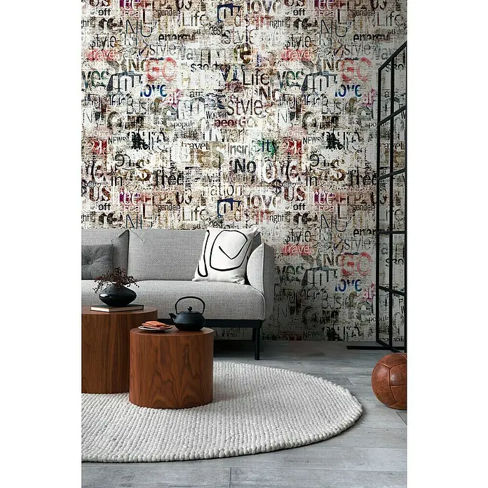A.S. Création The Wall 3 Fototapete Schriftzug - B x H: 159 x 280 cm, Vlies - Nahaufnahme eines stilvollen Wohnzimmers mit einem grauen Sofa, Holztischen und einem runden Teppich vor einer Wand mit Zeitungsmuster.