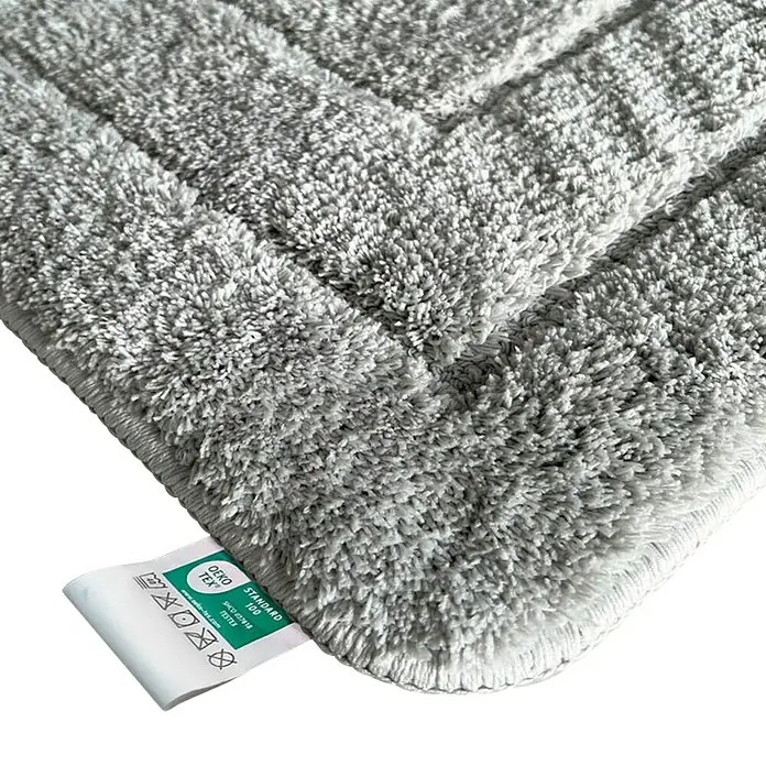 Floordirekt Badteppich Atlantis - 100 x 60 cm, Silbergrau, 100% Polyester - Nahaufnahme einer grauen Badematte mit OEKO-TEX Standard 100 Etikett, die die Qualität und Sicherheit des Produkts hervorhebt.