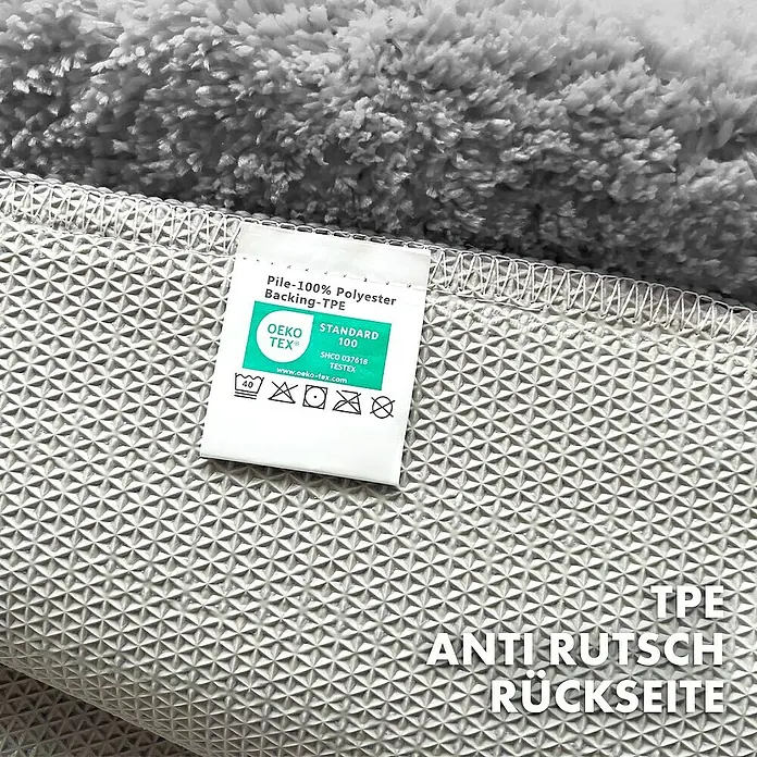 Floordirekt Badteppich Maris - 150 x 80 cm, Silber, 100% Polyester - Detailansicht der rutschfesten Rückseite eines grauen Teppichs mit Pflegeetikett.