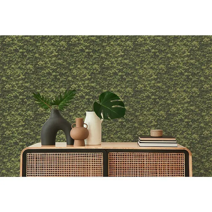 A.S. Création Pintwalls 2 Vliestapete Mooswand - Grün, Floral, 10,05 x 0,53 m - Detailaufnahme eines skandinavisch inspirierten Sideboards mit Rattanfront, dekoriert mit Vasen und Büchern, vor einem grünen Mooshintergrund.