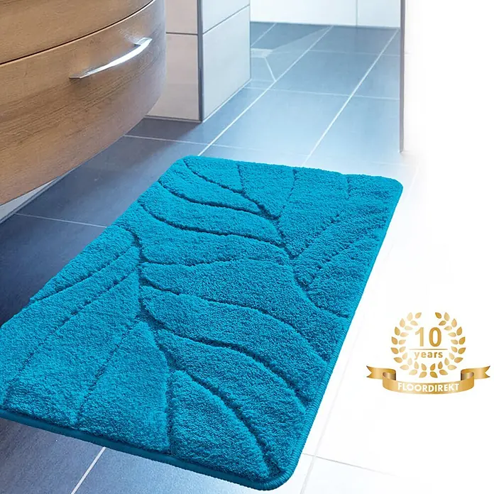 Floordirekt Badteppich Maris - 120 x 60 cm, Türkis, 100% Polyester - Eine blaue Badematte mit Blattmuster liegt vor einem Waschtisch. Sie ist flauschig und saugfähig.
