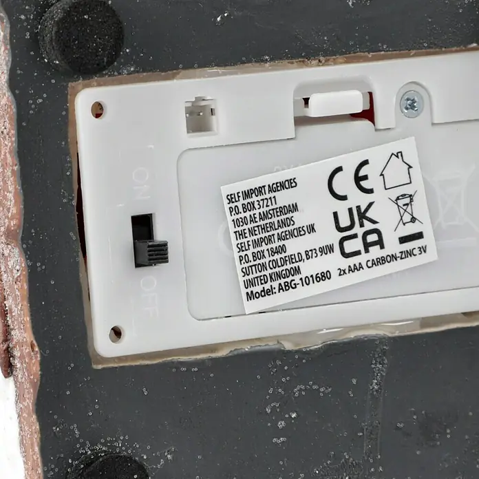 LED-Weihnachtsdorf Lebkuchenhaus - 9,5 x 9,5 x 13 cm, LED, Batteriebetrieben - Nahaufnahme der Unterseite eines Produkts mit Batteriefach, CE-Kennzeichnung und Informationen zu Hersteller und Stromversorgung.