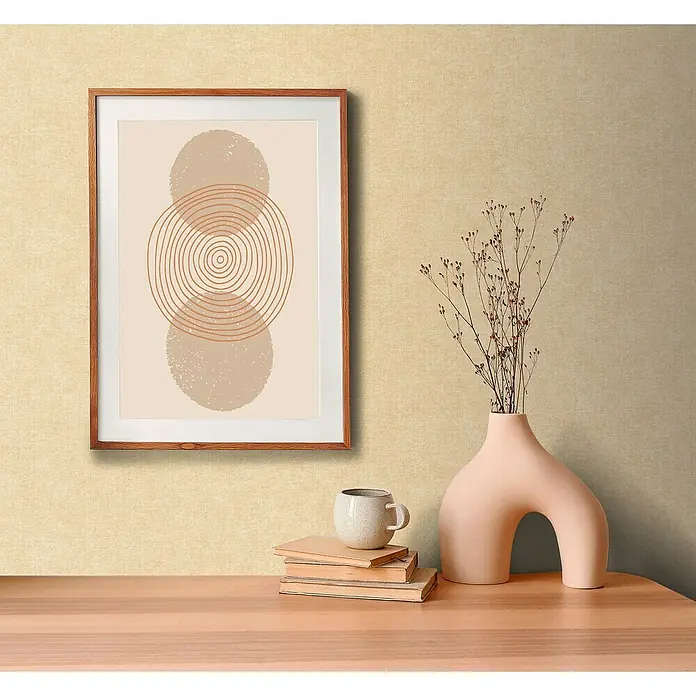 A.S. Création Metropolitan Stories Hot Spots Vliestapete - Beige, Uni, 10,05 x 0,53 m - Ein gerahmtes, abstraktes Kunstwerk mit Kreisen hängt über einem Tisch mit Büchern, einer Tasse und einer stilvollen Vase mit Trockenblumen.