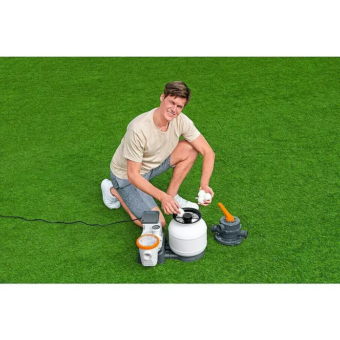 Bestway Flowclear Filterbälle - 500 g - Ein Mann kniet neben einer Poolfilteranlage auf Gras und füllt sie mit Filterbällen. Die Anlage ist weiß und grau mit orangefarbenen Akzenten.
