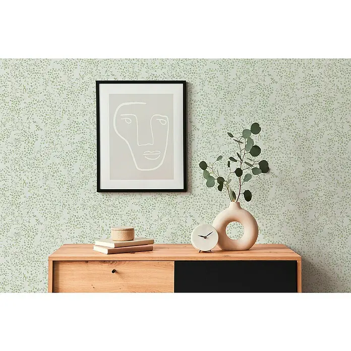 A.S. Création Pintwalls 2 Vliestapete Blumen - Grün-Weiß-Creme, Floral, 10,05 x 0,53 m - Nahaufnahme einer Kommode mit Dekor wie einem Bild und einer Vase, vor einer Wand mit Blättertapete.