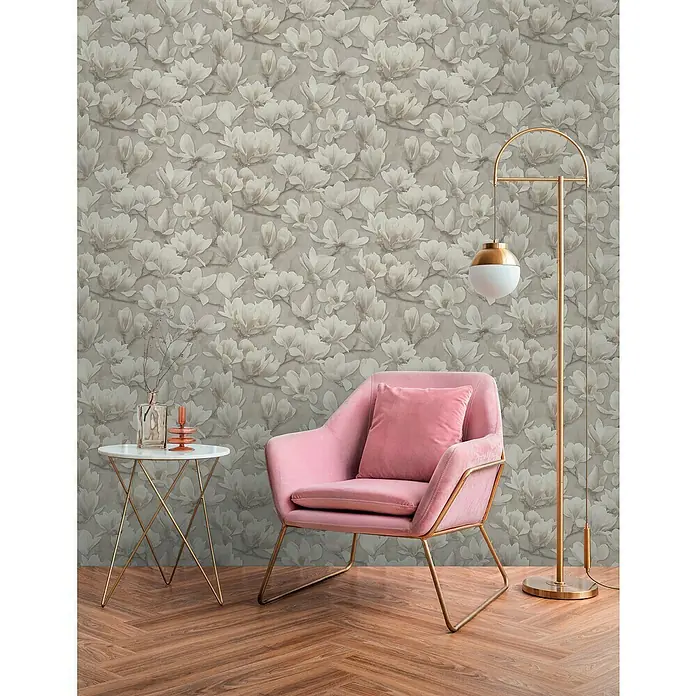 A.S. Création Pintwalls 2 Vliestapete Magnolien - Beige-Creme-Weiß, Floral, 10,05 x 0,53 m - Ein rosa Sessel mit goldenem Gestell, ergänzt durch eine Stehlampe und einen Beistelltisch, vor einer floralen Tapete.