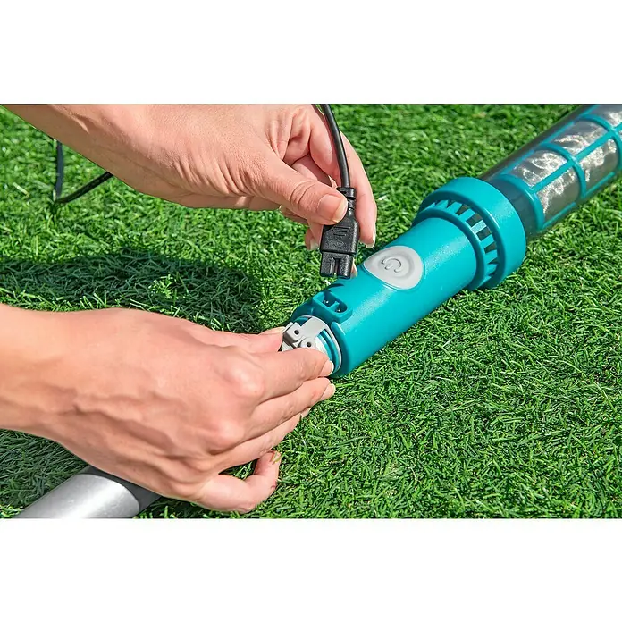 Bestway Poolsauger-Set AquaSurge - Türkis - Jemand schließt den Stecker eines türkisfarbenen Poolreinigers an, der auf einem grünen Rasen liegt.