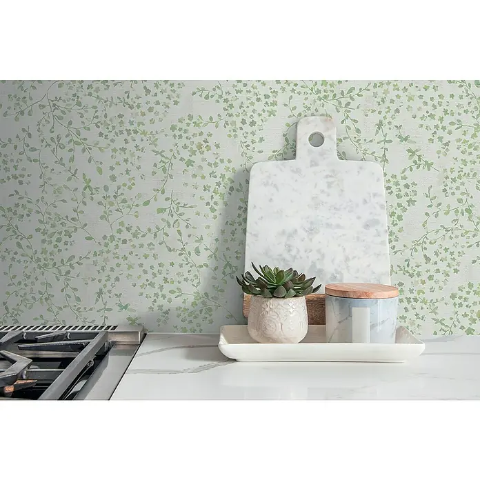 A.S. Création Pintwalls 2 Vliestapete Blumen - Grün-Weiß-Creme, Floral, 10,05 x 0,53 m - Elegante Marmor-Schneidebrett und dekorative Accessoires auf einer Küchentheke mit grünem Blättertapeten-Hintergrund.