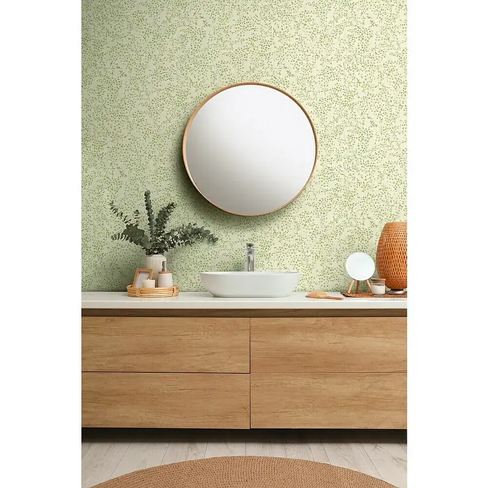 A.S. Création Pintwalls 2 Vliestapete Blumen - Grün-Weiß-Creme, Floral, 10,05 x 0,53 m - Ein Badezimmer mit einem stilvollen, hölzernen Waschtisch, einem runden Spiegel und einer dezenten grünen Blättertapete.